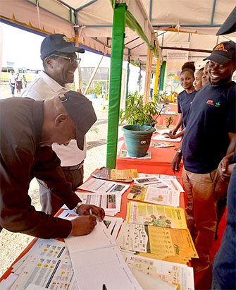 TARI Director General, Dr Geoffrey Mkamilo standing and TARI Board Chairman, Dr Yohane Bulena signing the visitors’ book at the IITA exhibition booth.